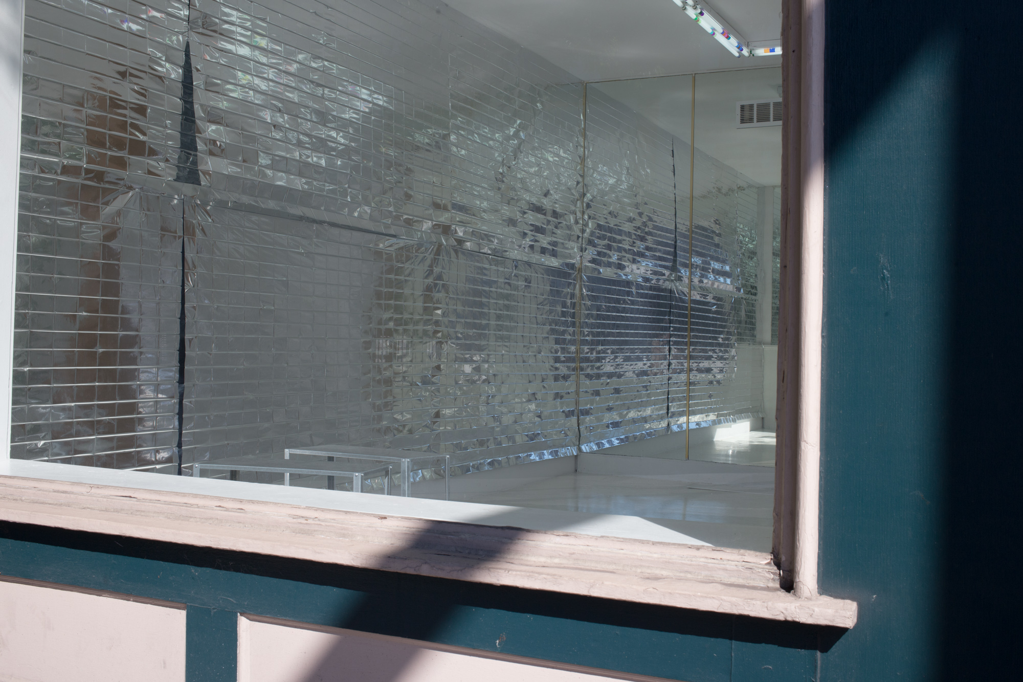 View through a large storefront window of reflective mylar with rectangular creases hanging on a wall