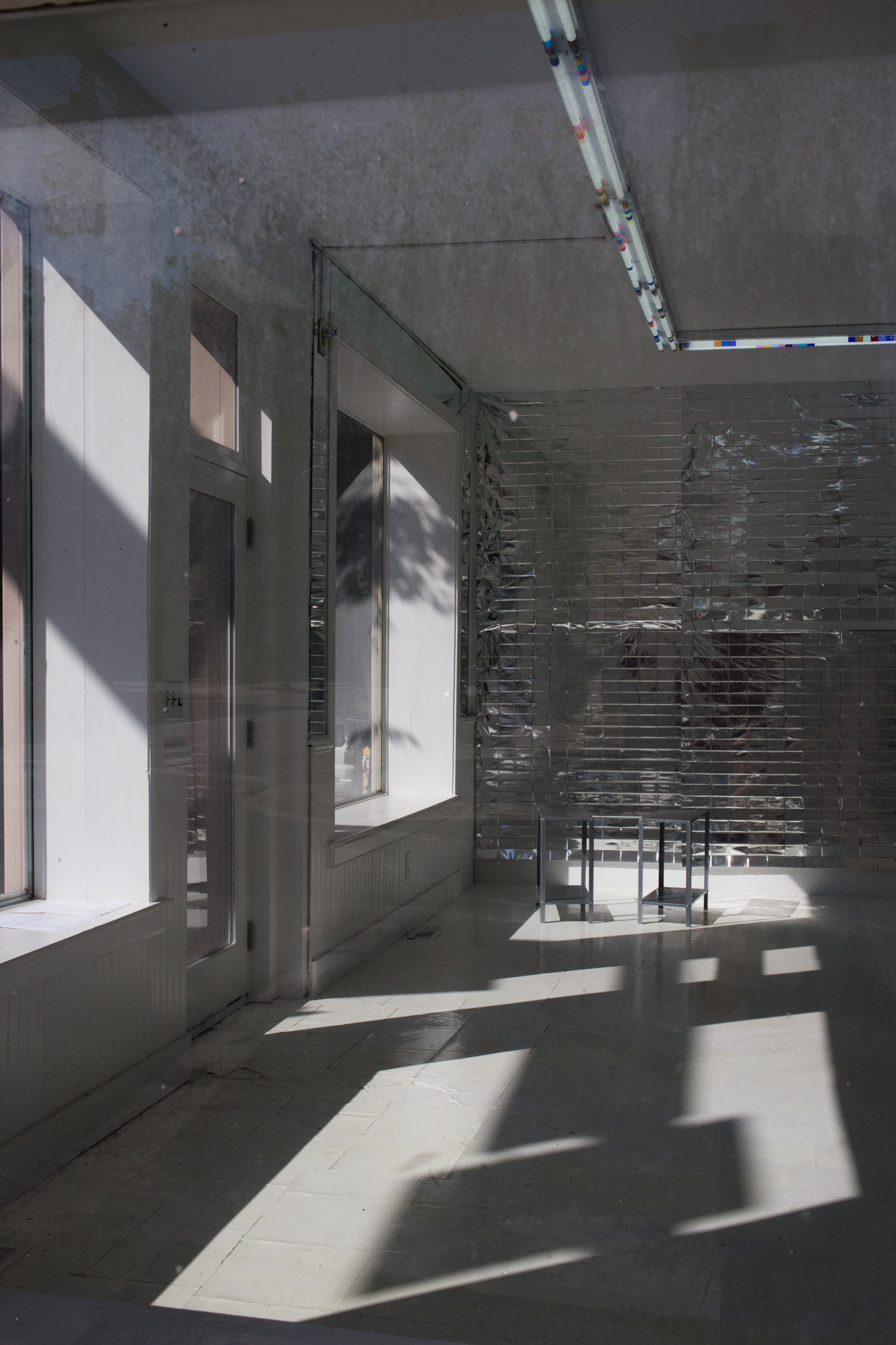 View through a window of reflective mylar hanging on a wall, with a pair of small metal tables in the foreground