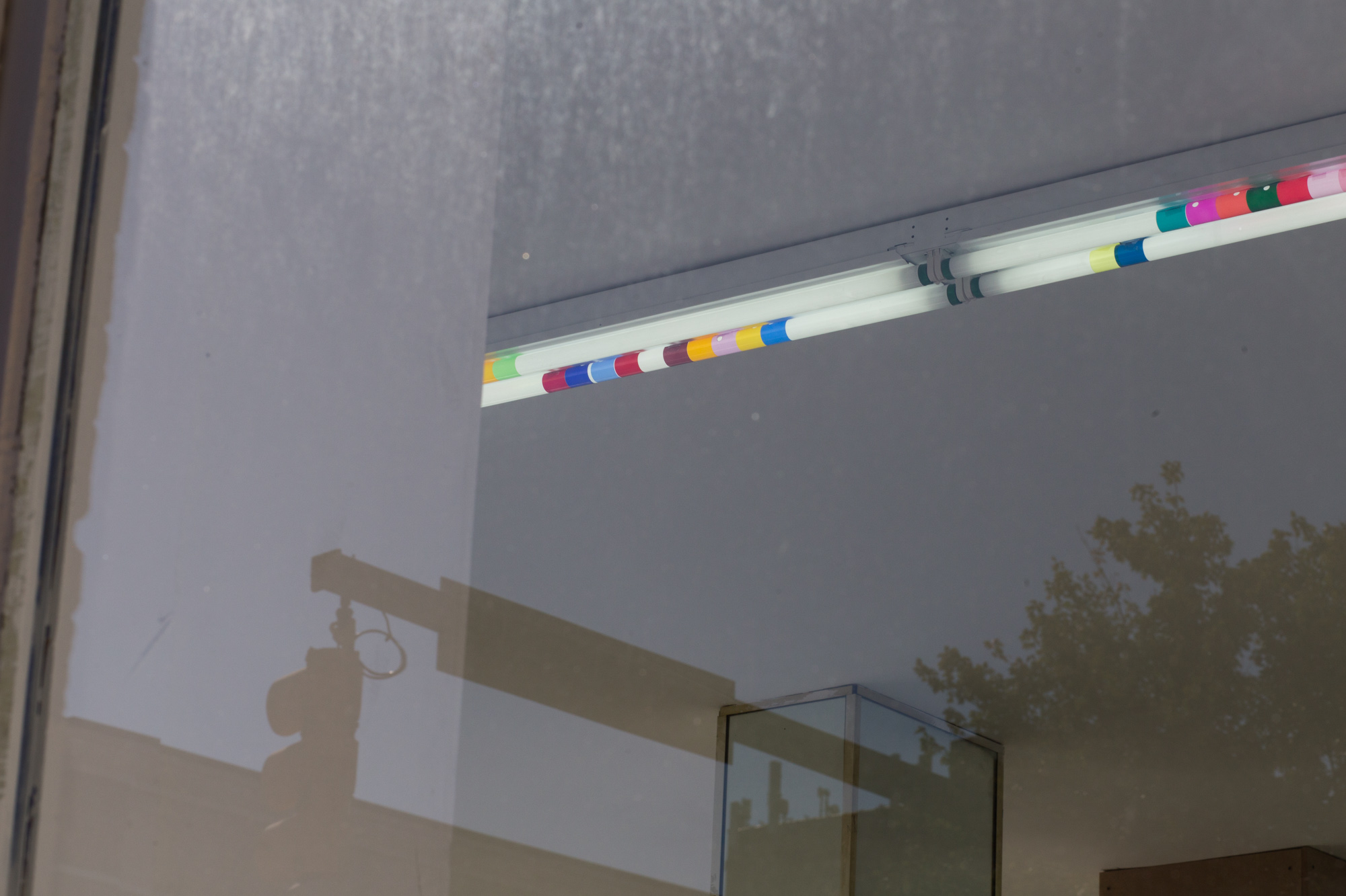 View through a window of fluorescent lights wrapped with colorful plastic; the is a traffic light reflected in the window