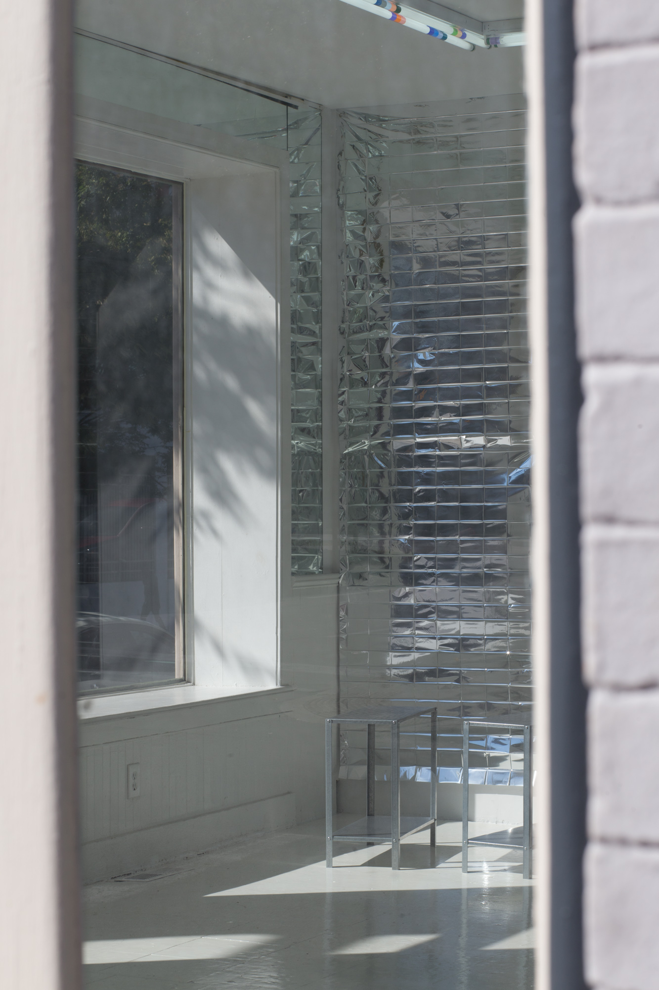 View through a window of reflective mylar hanging on a wall, with a pair of small metal tables in the foreground