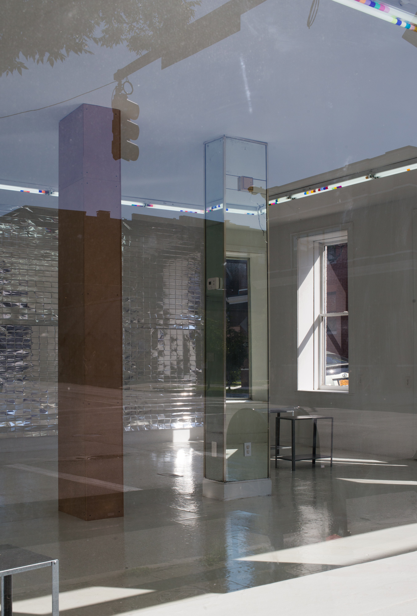 View through a window of mylar hanging on a rear wall and two columns--one mirrored, one made of masonite--in the middle of the room