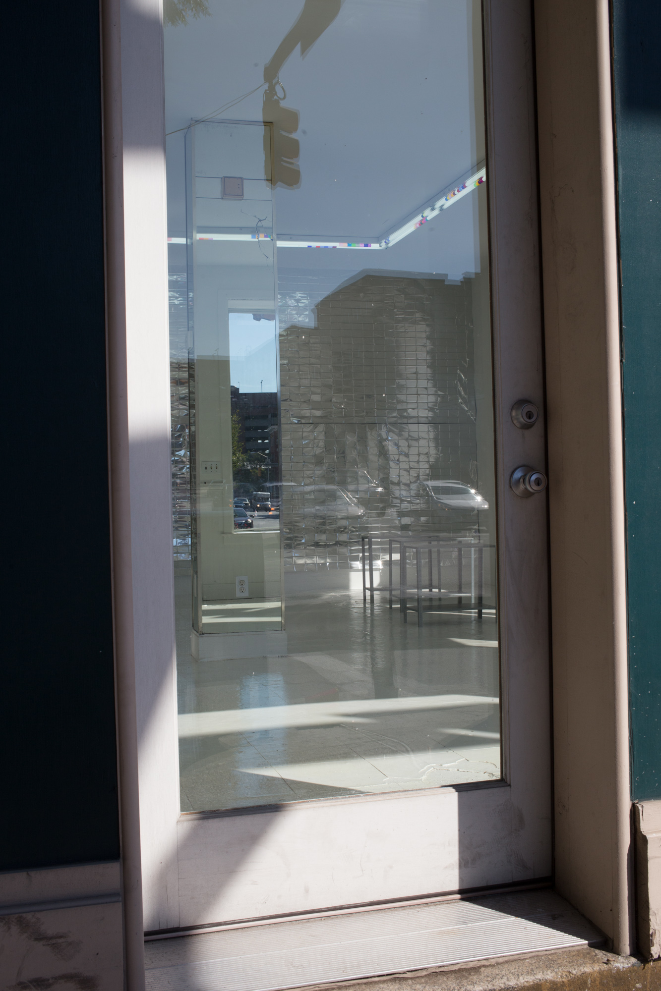 View through a glass storefront door of a mirrored column and small metal tables scattered inside