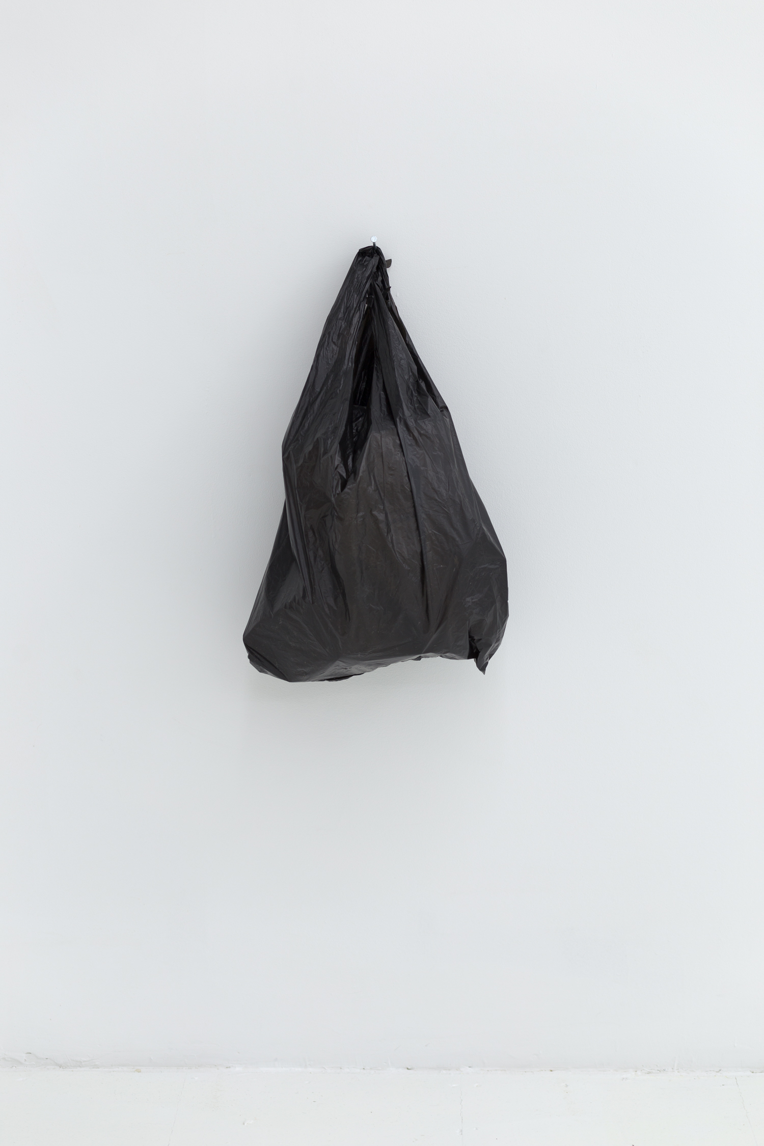 A black plastic bag hangs from a nail on a white wall