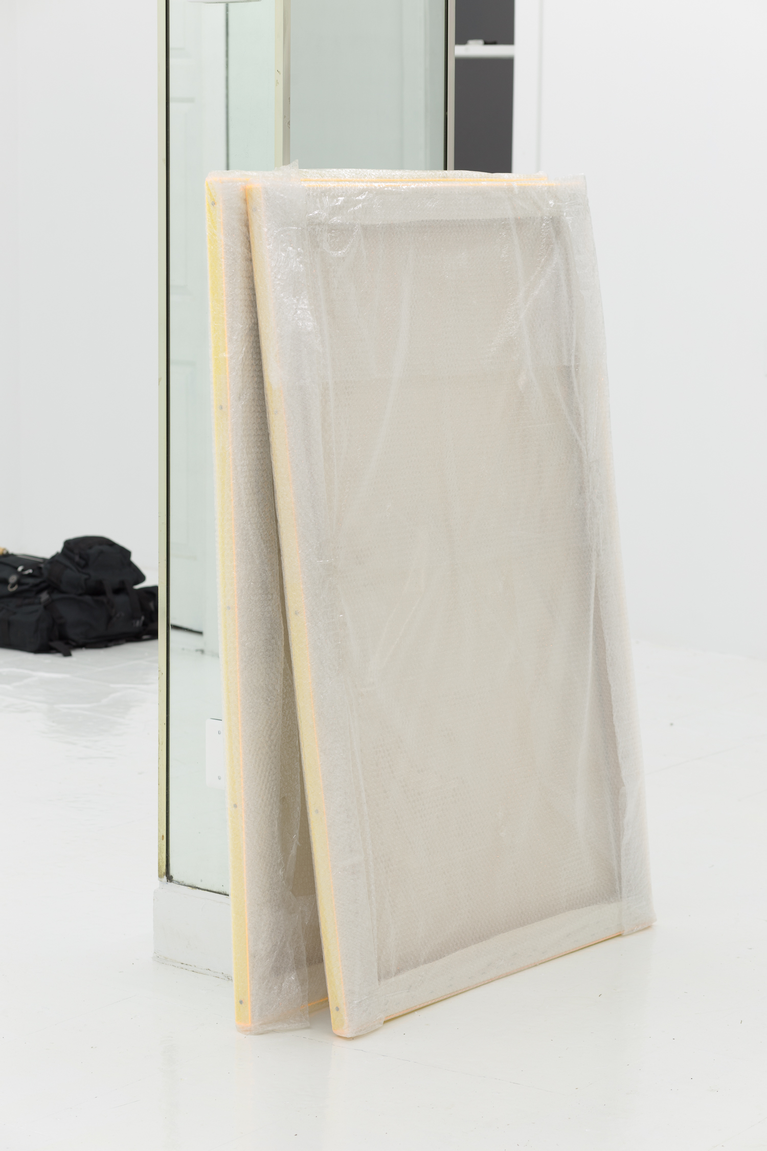 Paintings wrapped in plastic lean against a mirrored column