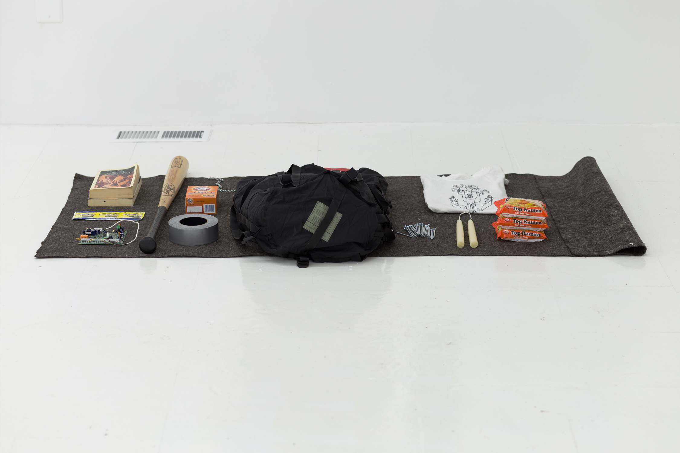 A piece of gray felt lies on the floor, spread with an assembly of items and a black backpack
