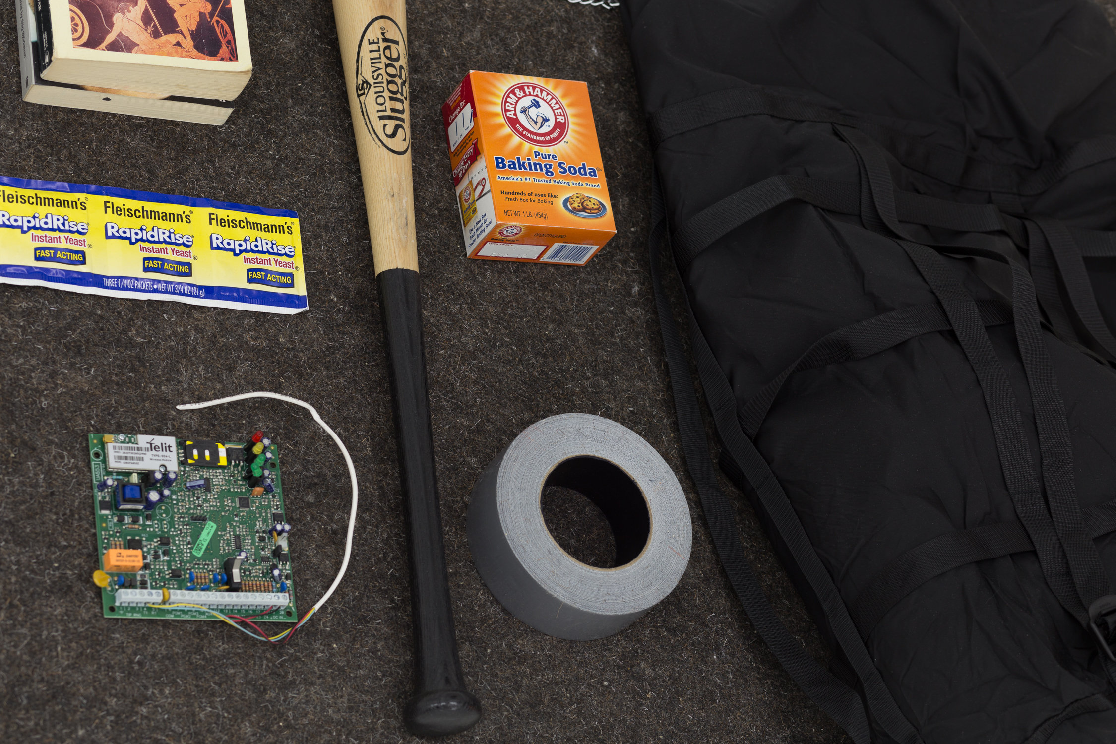 Items on gray felt: a carton of baking soda, a baseball bat, a roll of duct tape, a stack of books, computer parts, and several packets of RapidRise yeast
