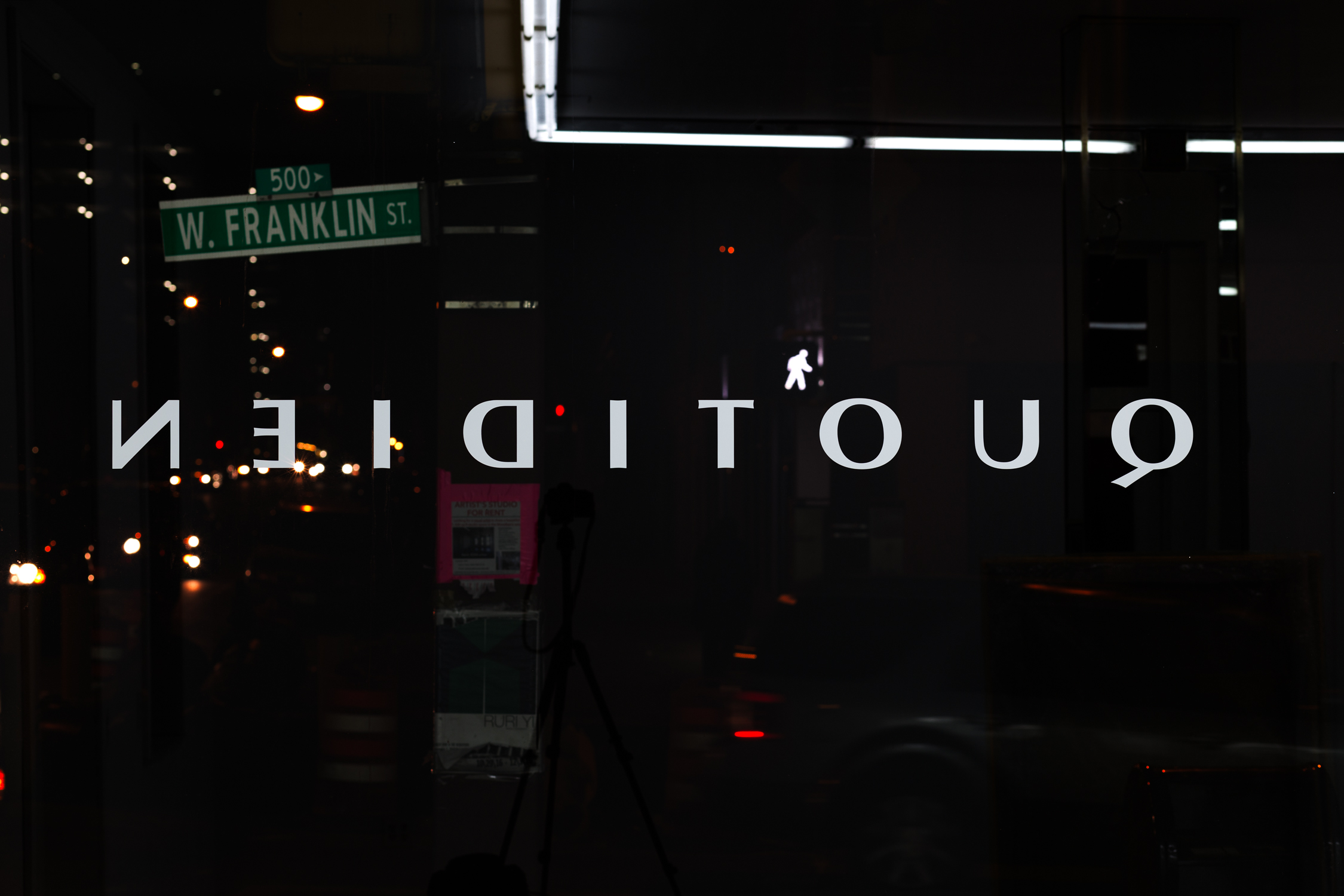 The window decal as viewed from inside the gallery looking out into the night: ‘quotidien’ backwards