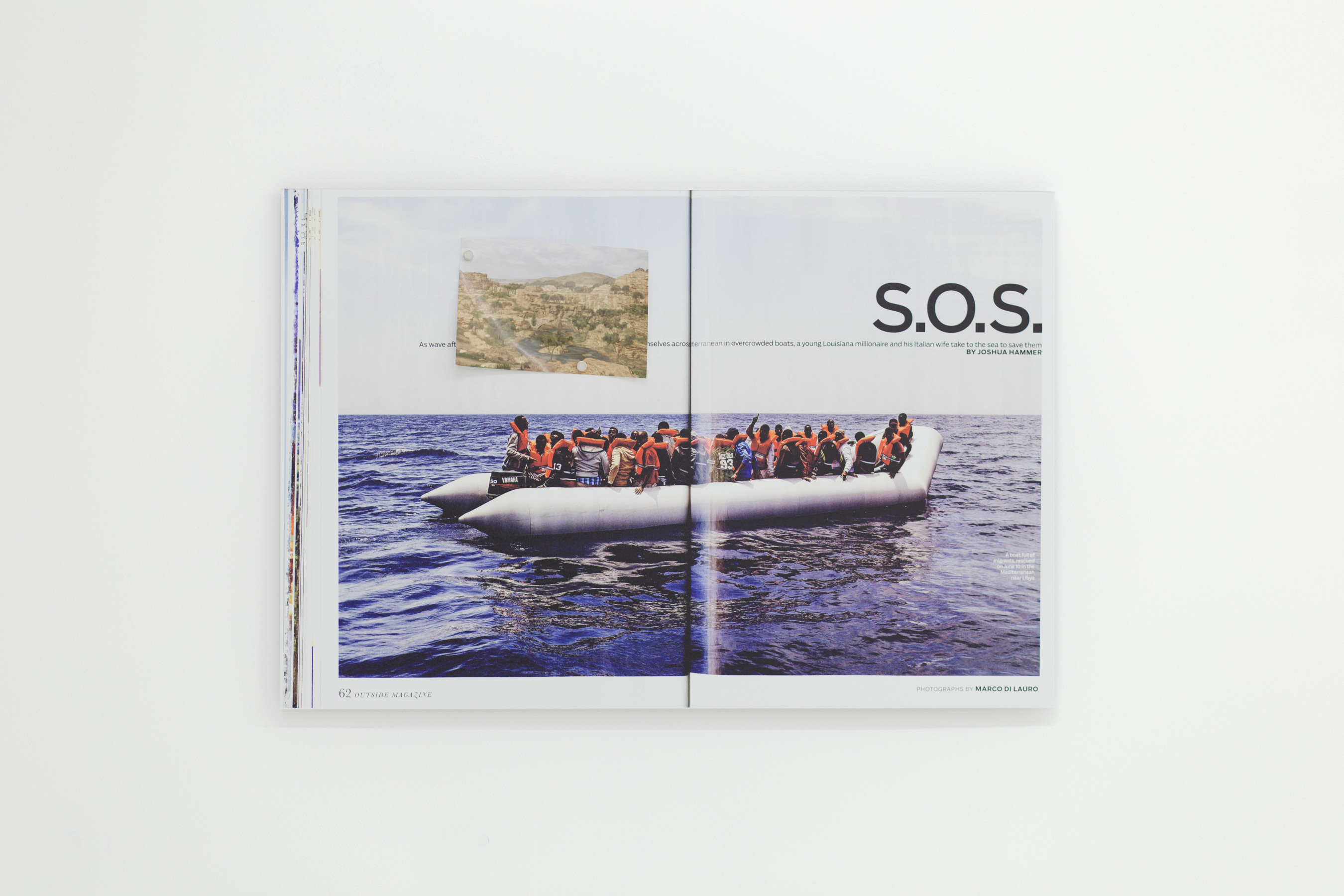 Print of a magazine spread on aluminum depicting people in life vests on a raft. There is a small photo attached to the print by magnet