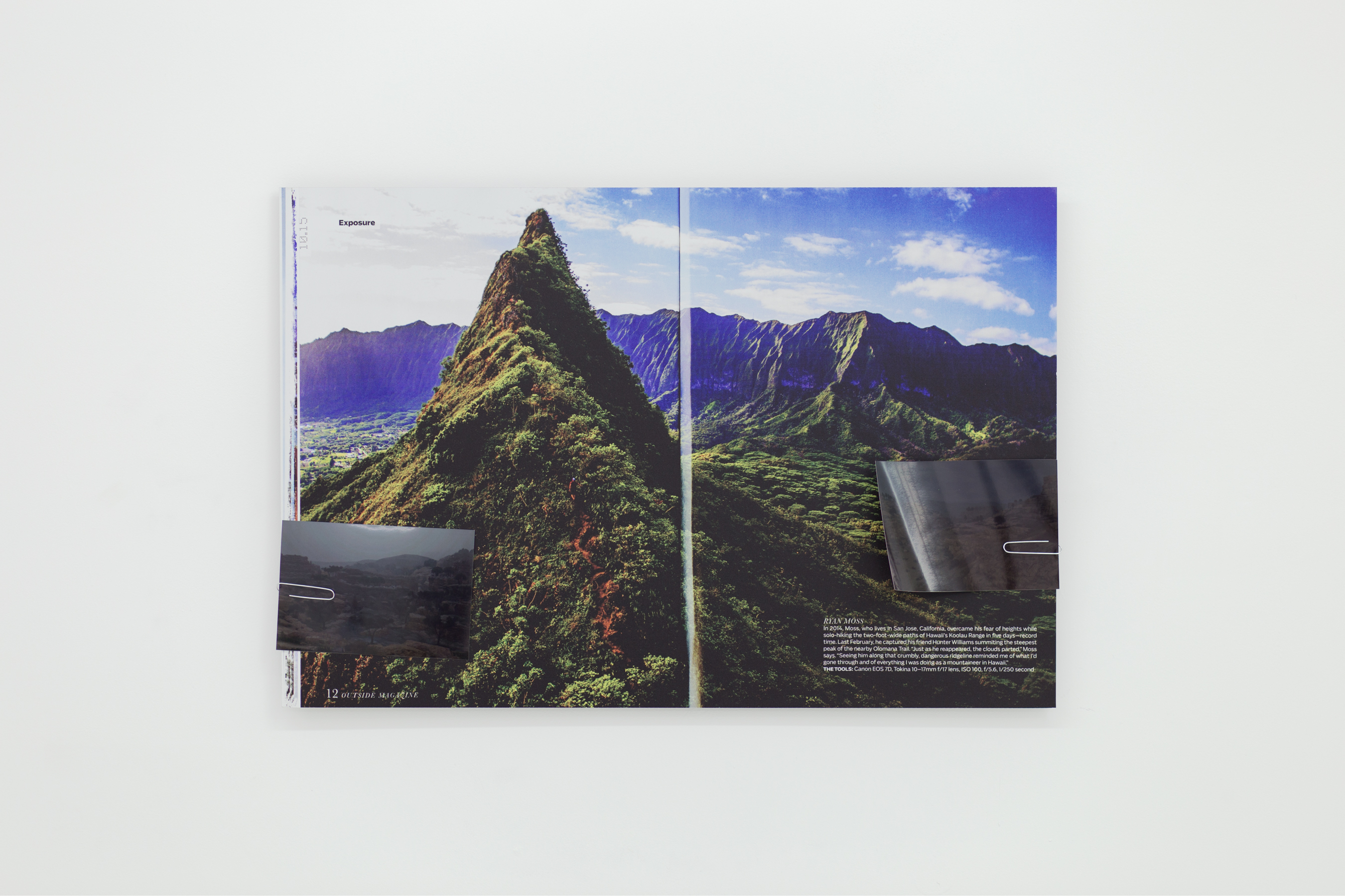 Print of a magazine spread on aluminum depicting a lush mountainside. There are two small photos attached to the print by paperclips