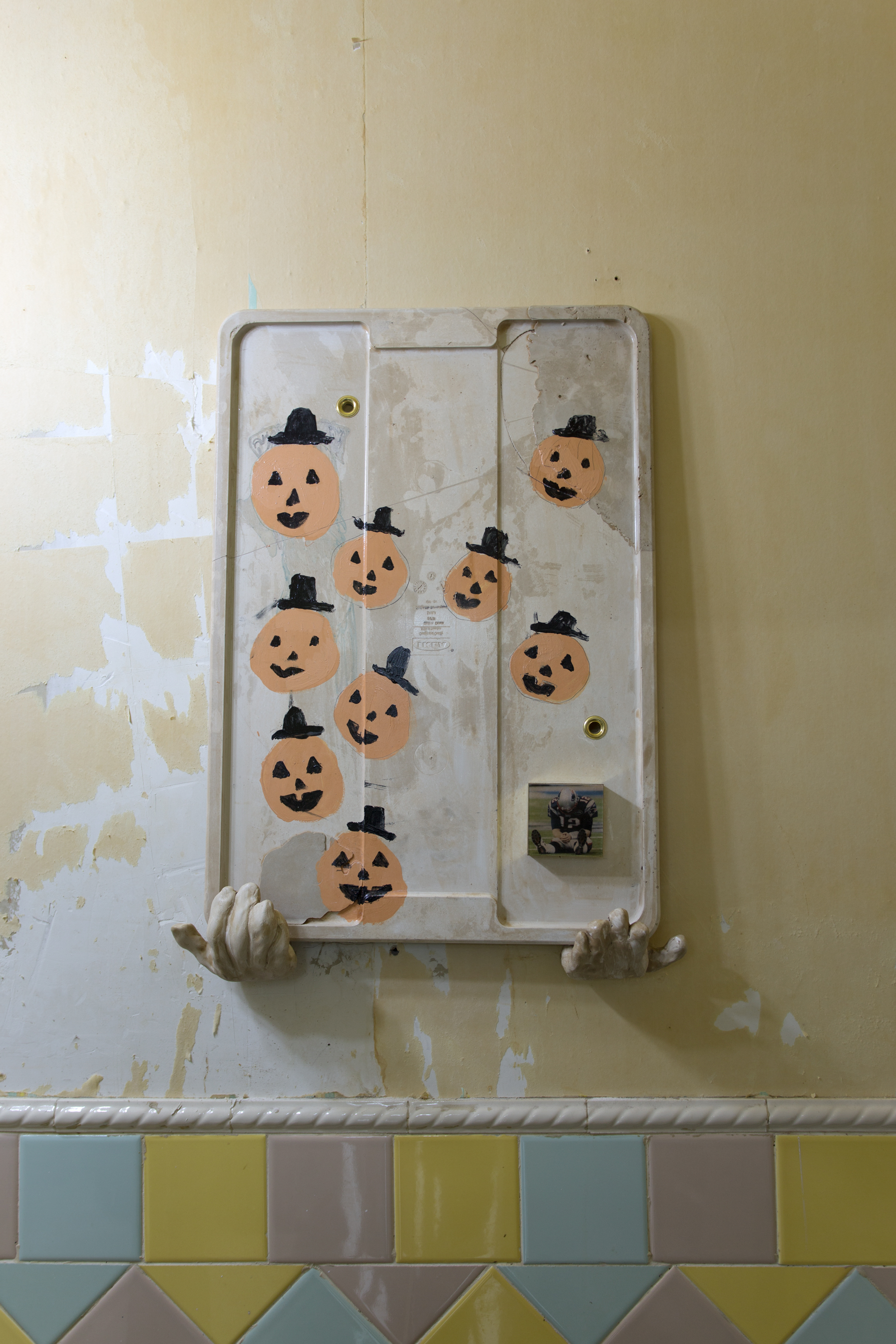 A concrete cast of a rubbermaid lid sits on two ceramic hands. It is painted with jack-o-lanterns, has a grommet, and a photo of a slumped football player