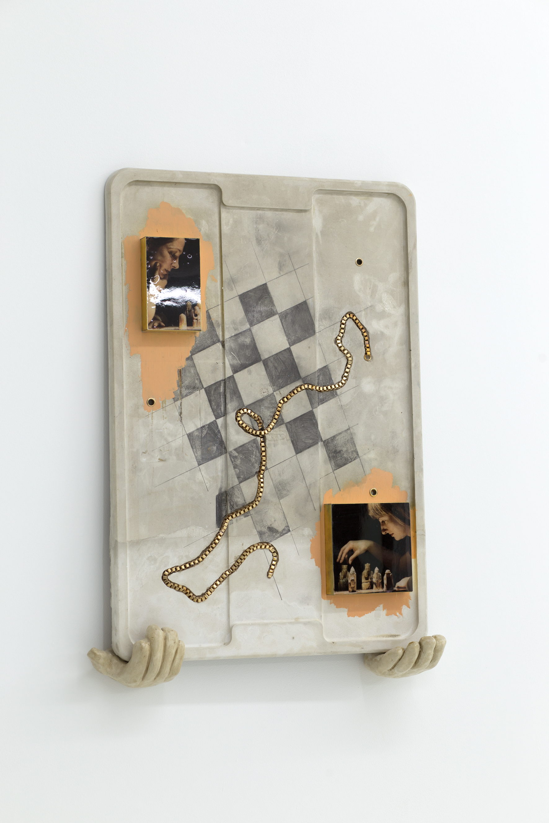 A concrete cast of a rubbermaid lid sits on two ceramic hands. It has a chess board sketched on its surface, and a necklace inset