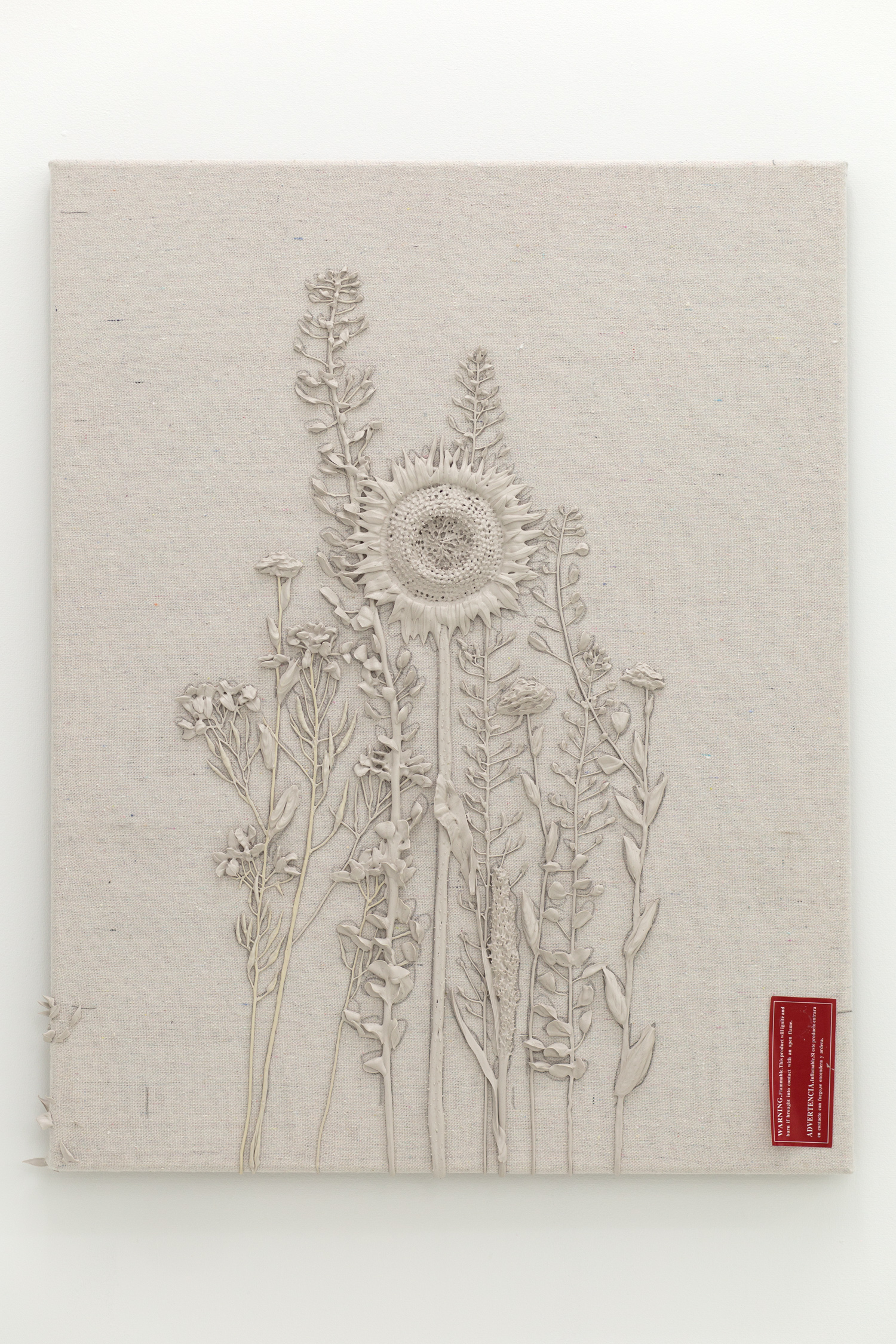Grey monotone plastic painting of one sunflower and assorted other plants; there is a red sticker in the lower right-hand corner