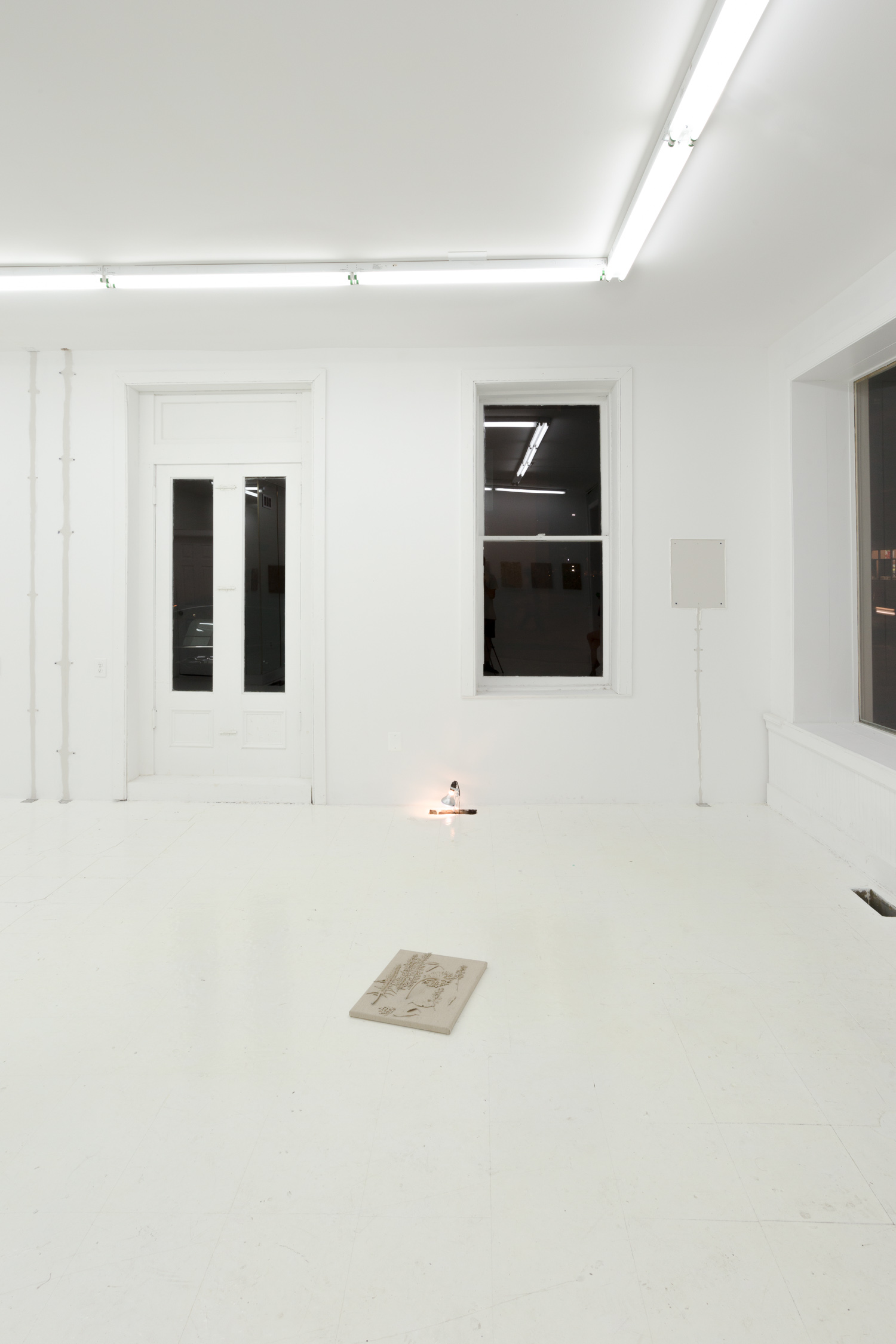 One of the paintings lies on the floor in the foreground. Behind it, a clamp light is pointed down into an open A/C vent in the floor
