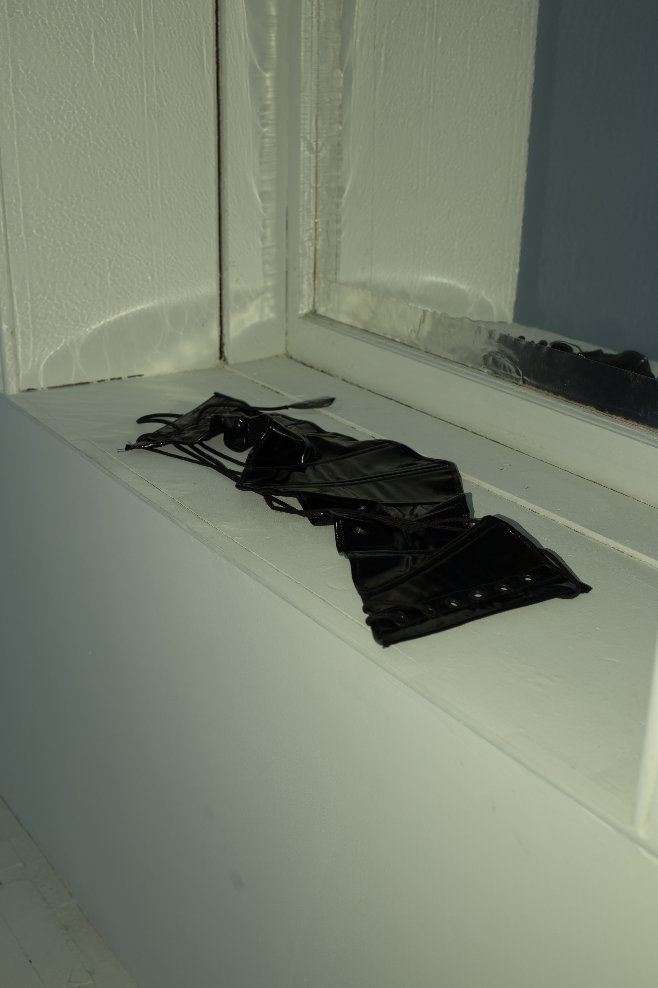 A corset lies in the windowsill, reflected in the mylar behind it
