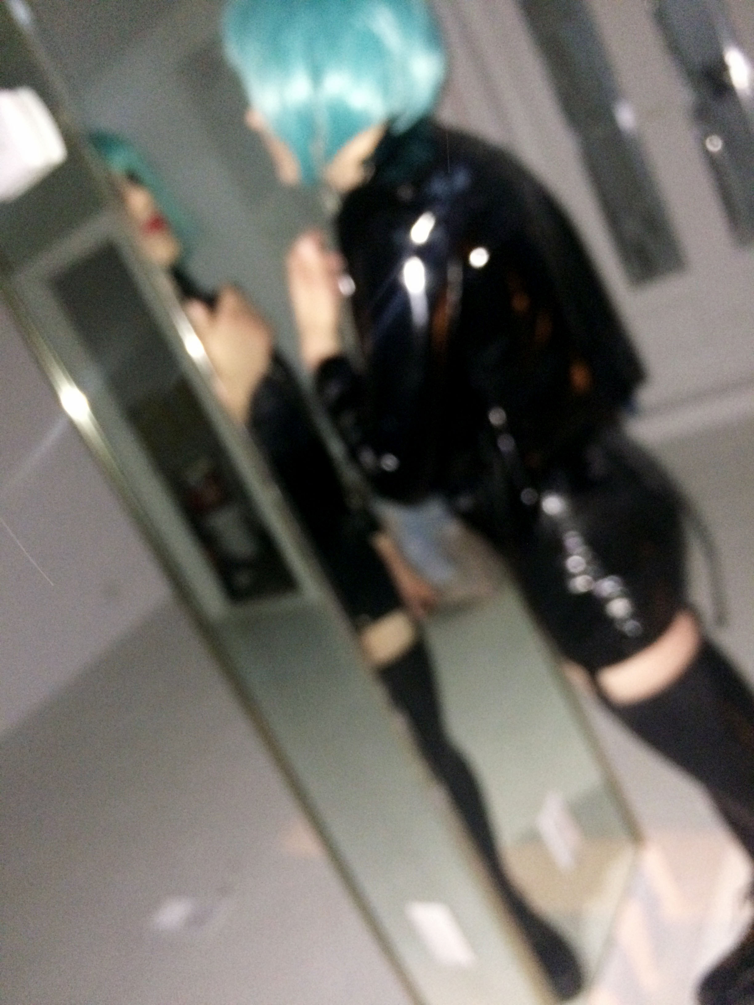 A blurry photo of a person in black latex and a blue wig looking at themselves in a mirror