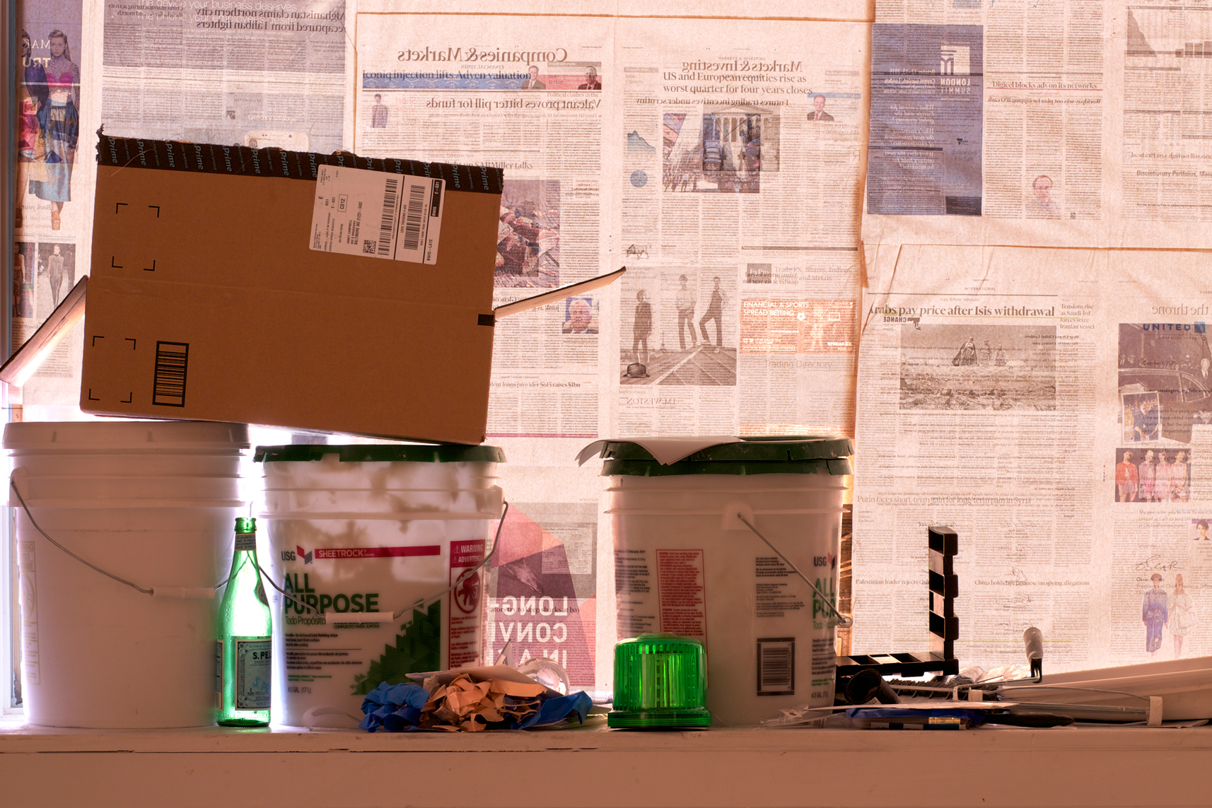 Buckets of joint compound, tools, and Amazon packaging sit in front of a window lined with Financial Times newspaper