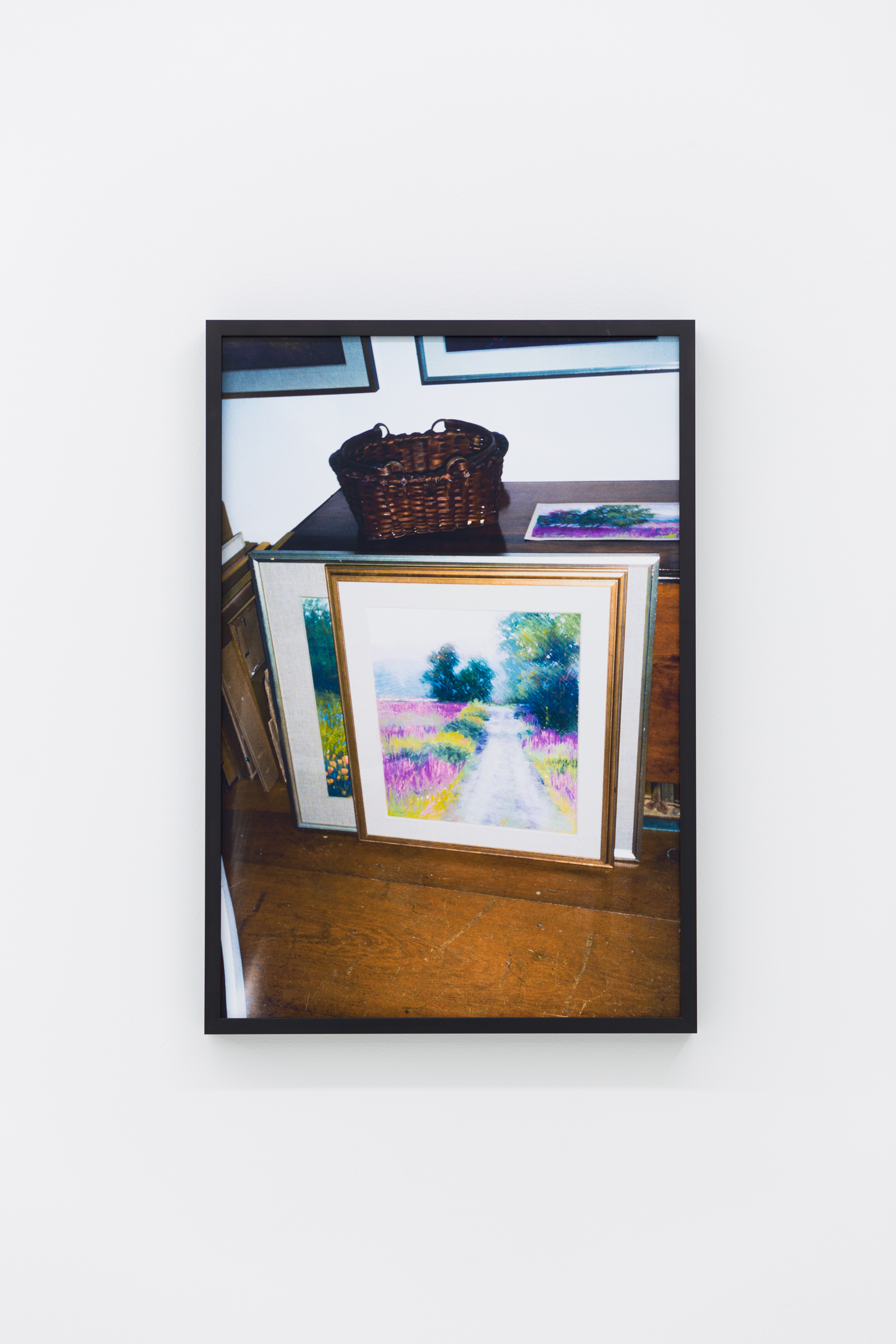 Photo of several paintings of flower-filled fields leaning against a table, on which sits a basket