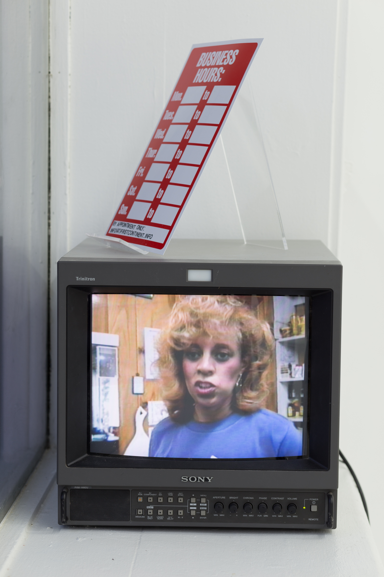 A CRT monitor sits in a windowsill with a blank business hours sign above it. It is playing the documentary short, “Diana’s Hair Ego