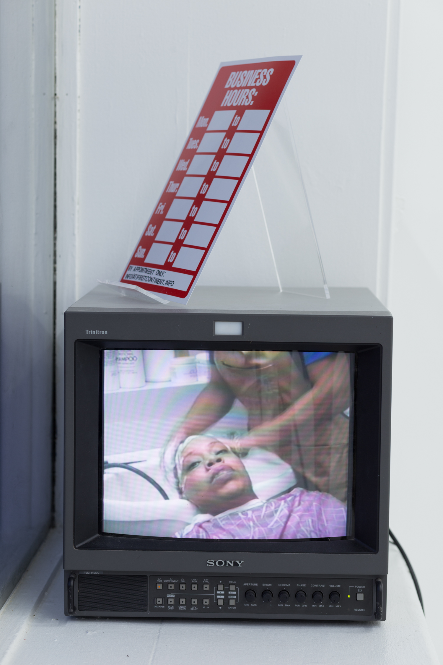 A CRT monitor sits in a windowsill with a blank business hours sign above it. It is playing the documentary short, “Diana’s Hair Ego
