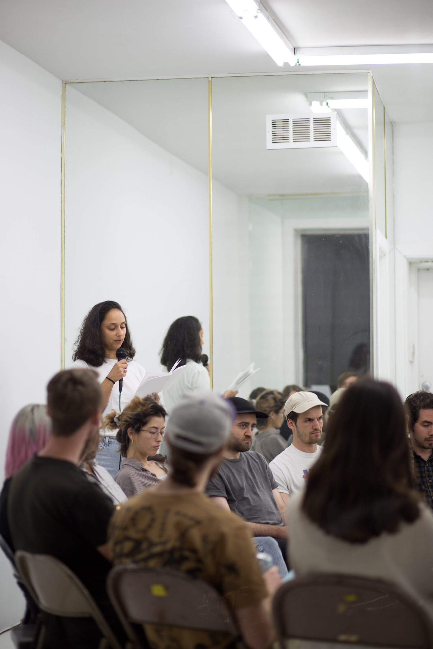 A performance by Ramaya Tegegne. She speaks into a microphone and the chairs are filled with listeners