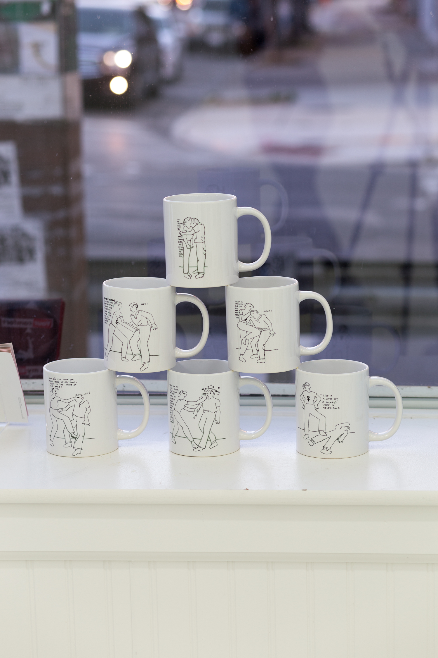 Mugs decorated with line drawings are stacked in a pyramid formation