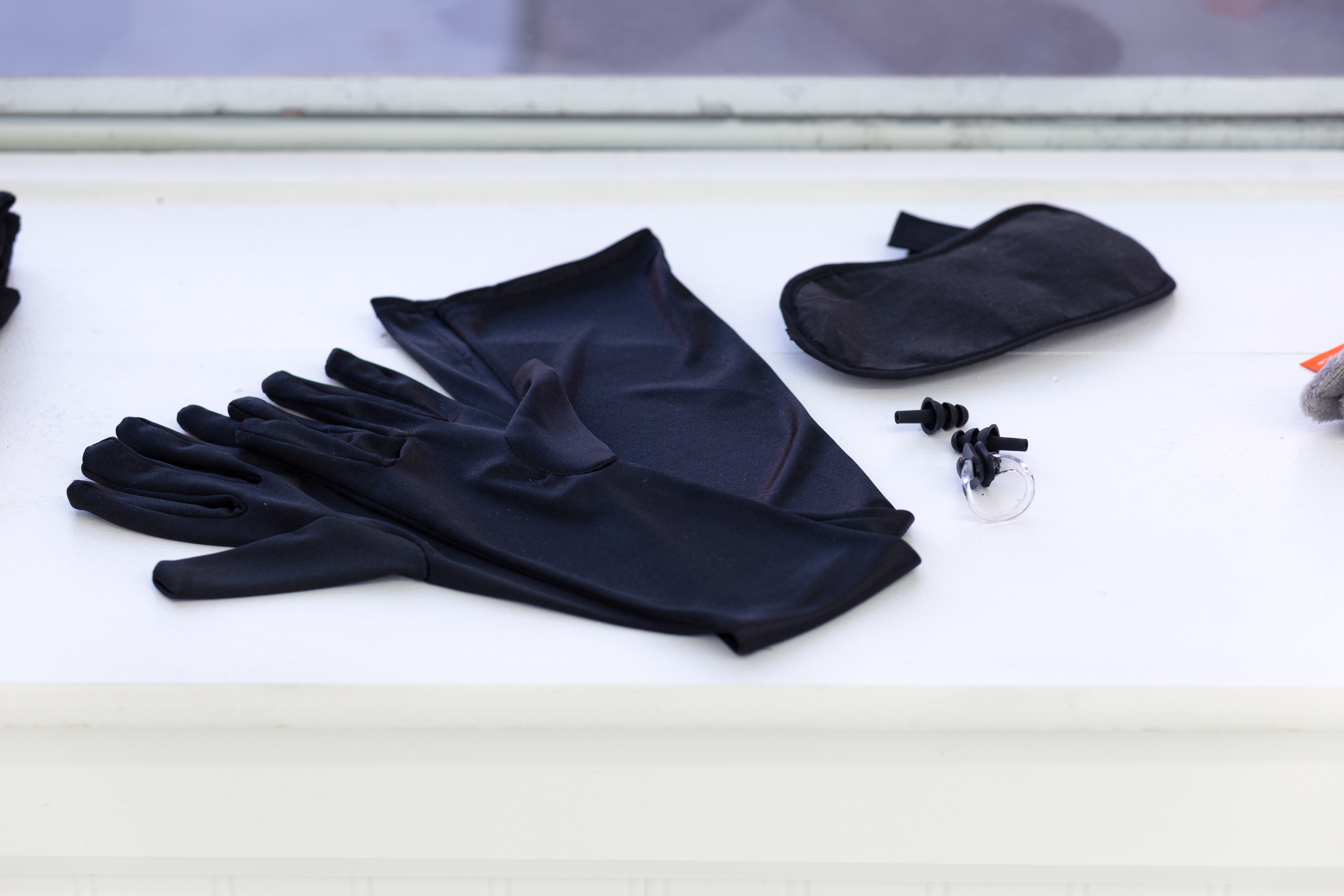 Black gloves, earplugs, a nose plug, and an eye mask sit in the windowsill